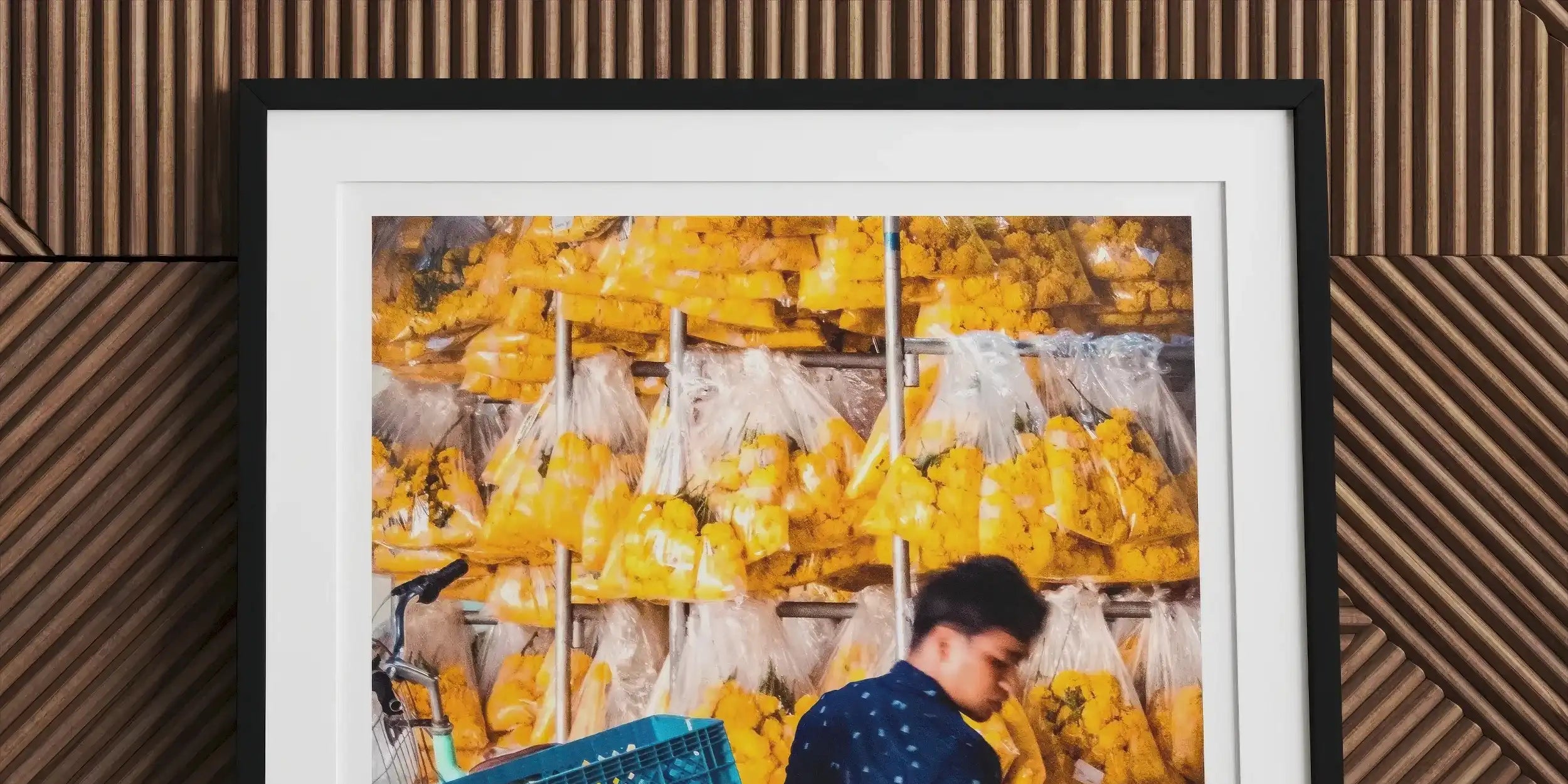 Framed photograph of a person handling produce in a market stall filled with yellow fruits or vegetables.