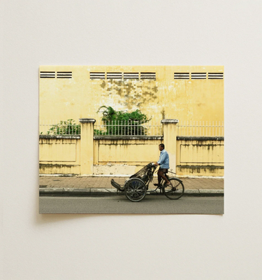 A framed photo of a man cycling a rickshaw past a yellow wall, representing urban life in concrete jungle art.