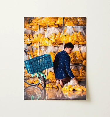 Photography Wall Art featuring a man arranging vibrant yellow produce in bags against a colorful backdrop.
