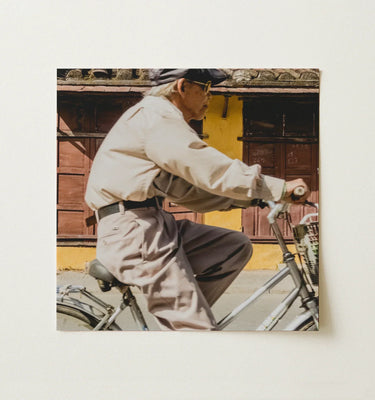 Vietnam Wall Art featuring a person riding a bicycle against a backdrop of rustic buildings.