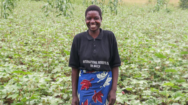 Someone wearing a black t-shirt and blue floral-patterned skirt stands with a bright smile