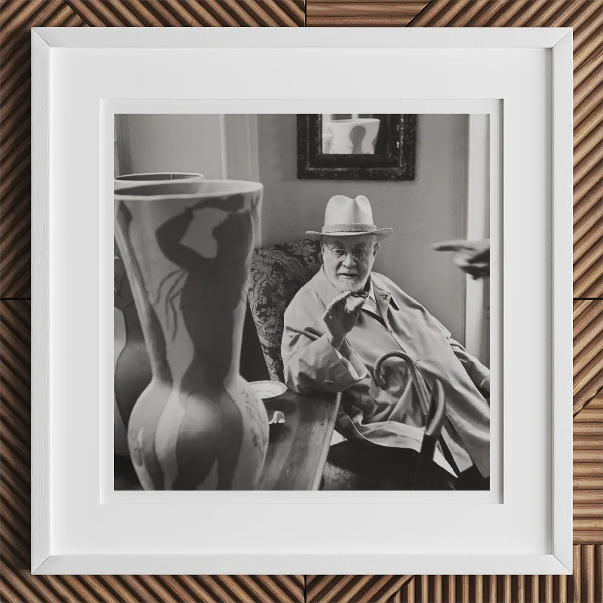 Black and white photo of an older man in a hat and trench coat with a large vase, inspired by Andy Warhol or Louise Bourgeois