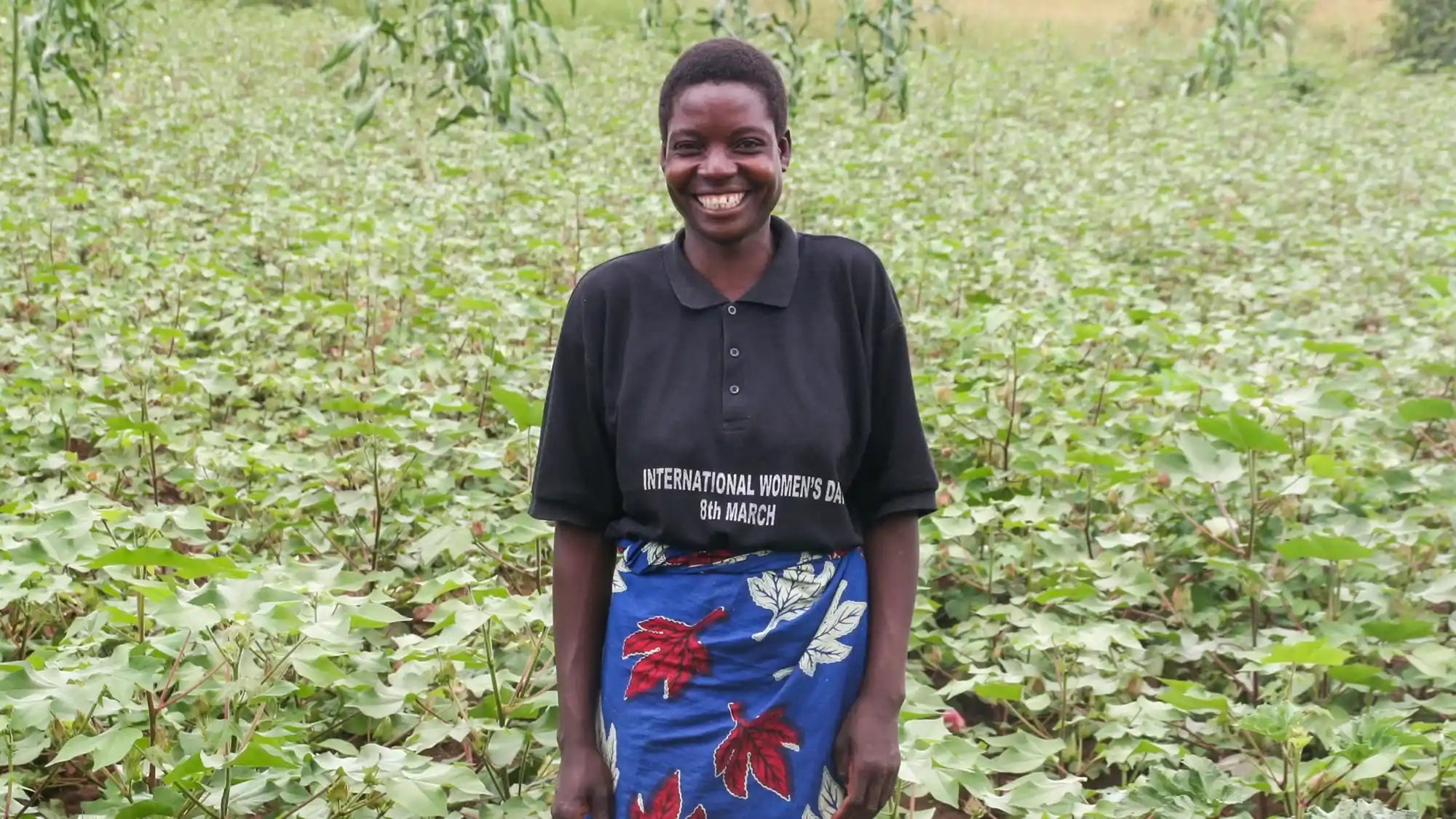 Someone wearing a black polo shirt and blue floral-patterned skirt standing in a field.