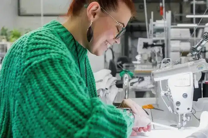 Someone wearing a bright green knit sweater works at a sewing machine.