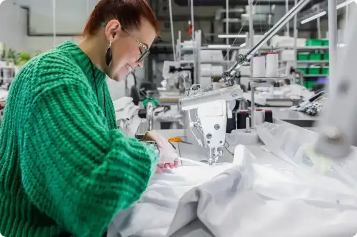 Someone wearing a bright green sweater working at a sewing machine.