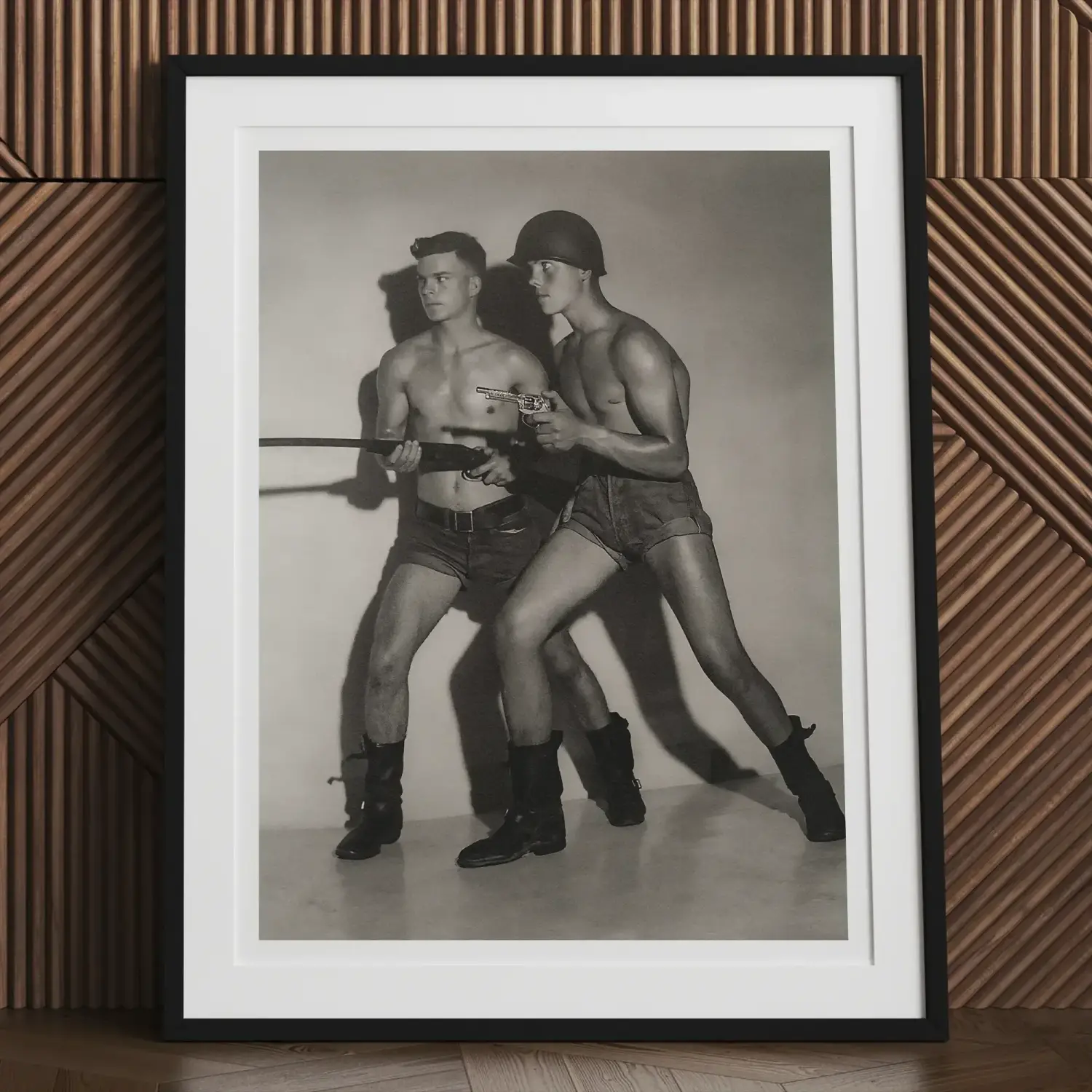 Framed black and white photograph of two shirtless men with guns in Bob Mizer’s queer chronicle
