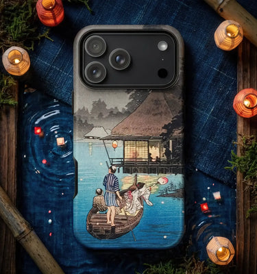 A phone case featuring a Japanese-style woodblock illustration of a boat scene by a river with a thatched-roof house, shown on a phone. The case is presented in a styled flat-lay setting with blue fabric, bamboo, moss, and glowing lanterns.