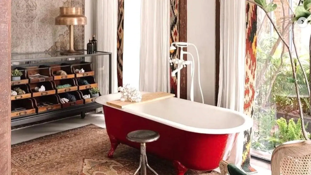 Red clawfoot bathtub as a statement piece in minimalist maximalist design.