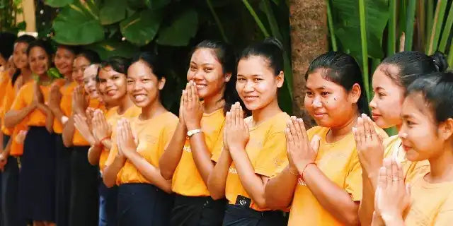 A row of people wearing yellow shirts with their hands pressed together in a prayer or greeting gesture.