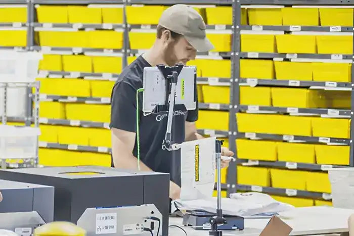 Warehouse worker processing packages at a sorting station with yellow storage shelves behind them.