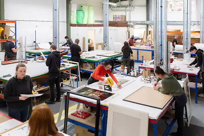 Workshop or studio space with multiple workstations where people are engaged in hands-on projects.